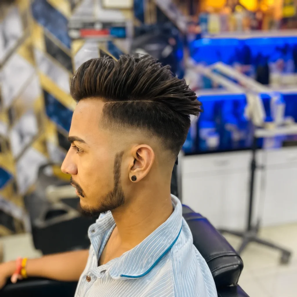 Potongan rambut high fade pompadour untuk pria, tampilan profil samping dengan bagian atas bervolume dan ditata rapi, fade tajam di sisi rambut, serta garis janggut yang bersih di dalam setting barbershop modern.