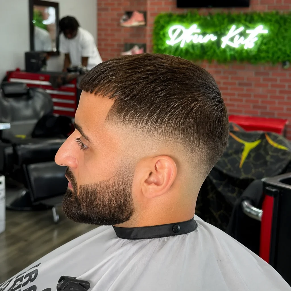 Potongan rambut clean low skin fade dengan bagian atas pendek bertekstur dan garis janggut yang tajam, gaya barber modern.