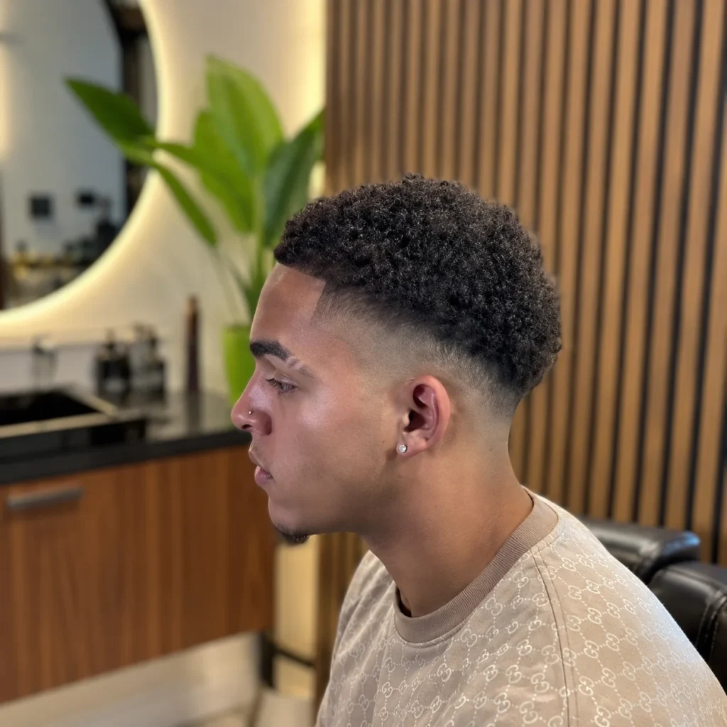 Potongan rambut high drop fade pada pria muda dengan taper fade yang tajam dan rambut keriting bertekstur, gaya rambut modern di barbershop yang stylish untuk pria – fadehaircut.blog